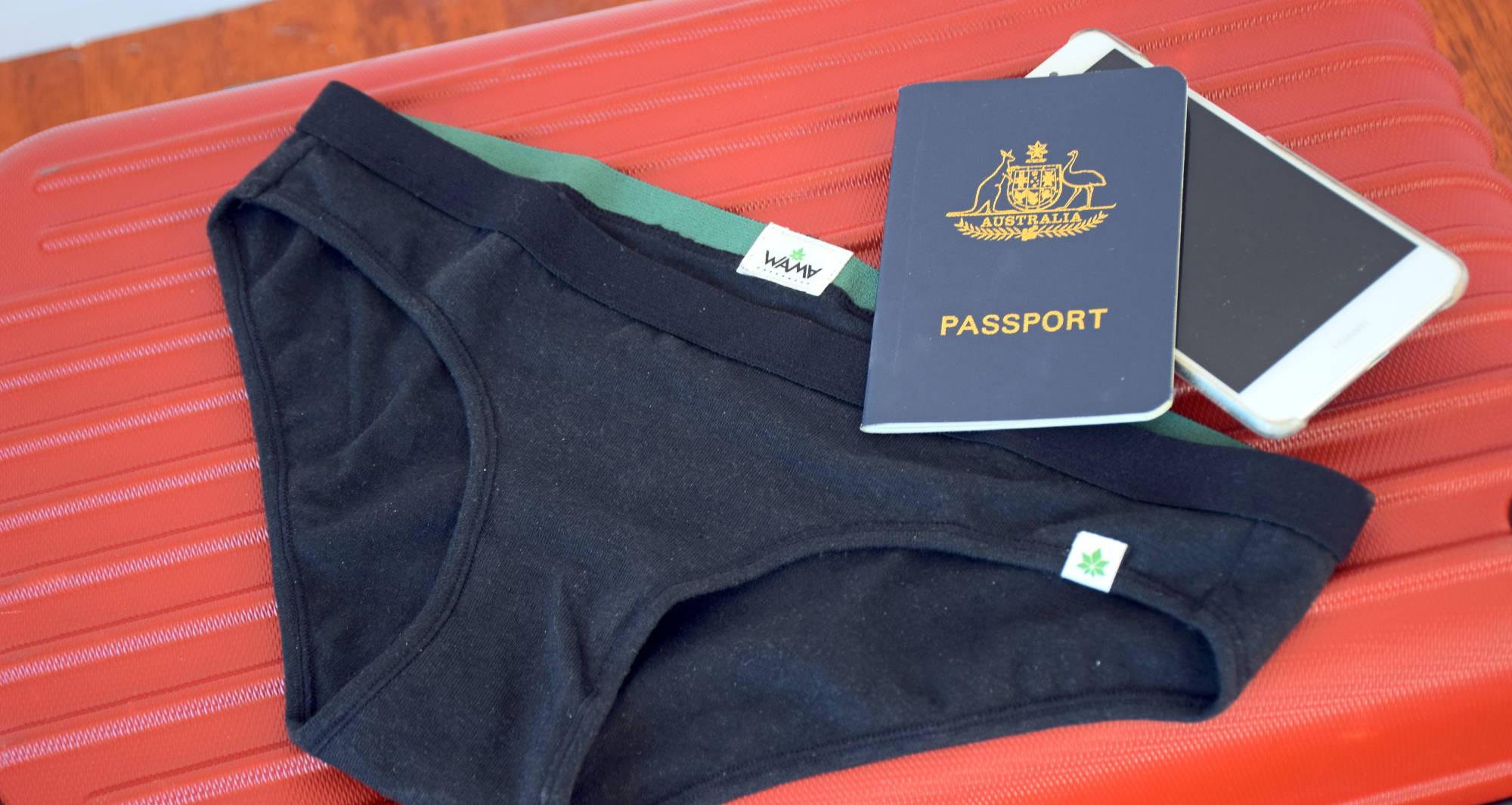 a pair of black underwear with a passport on top laid on an orange suitcase