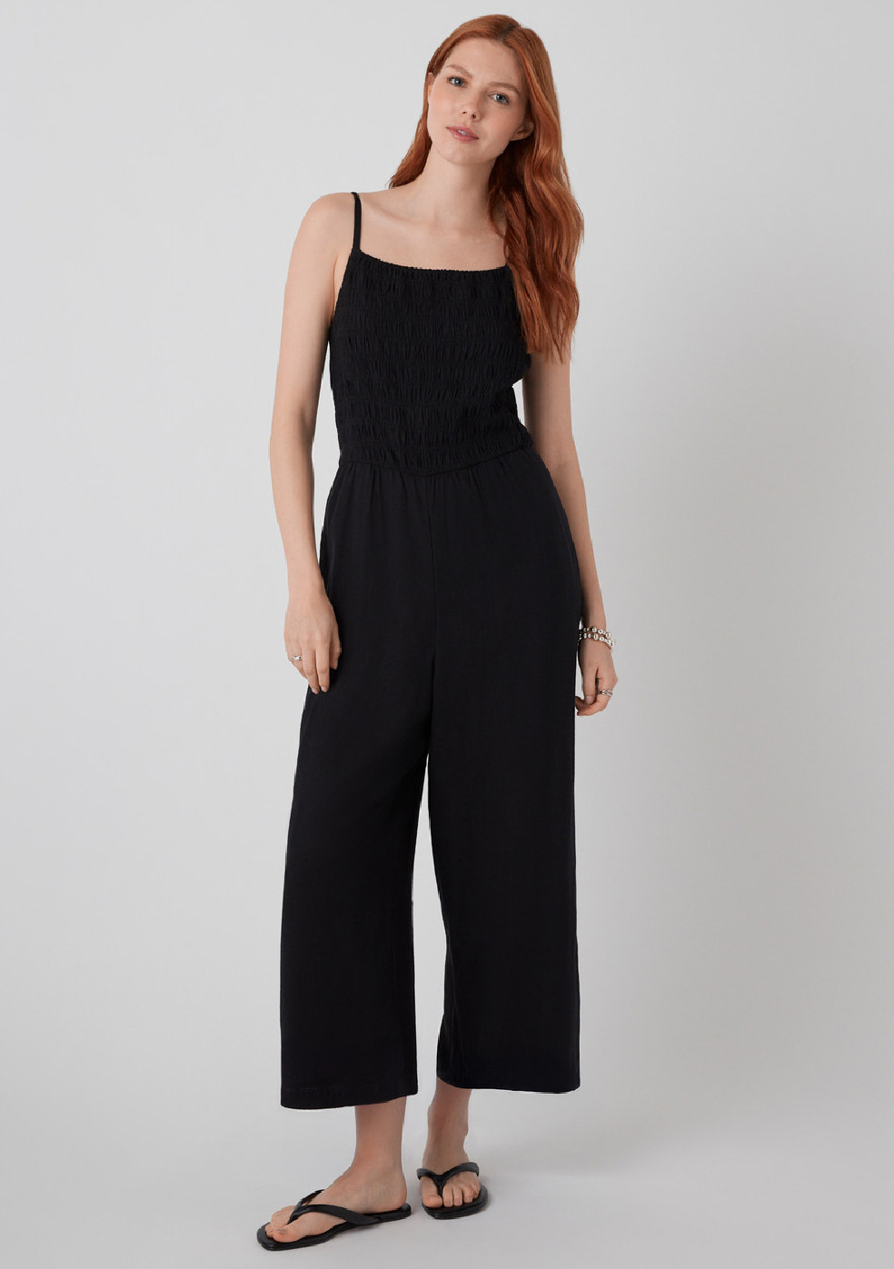 Woman in a black jumpsuit standing against a neutral background.