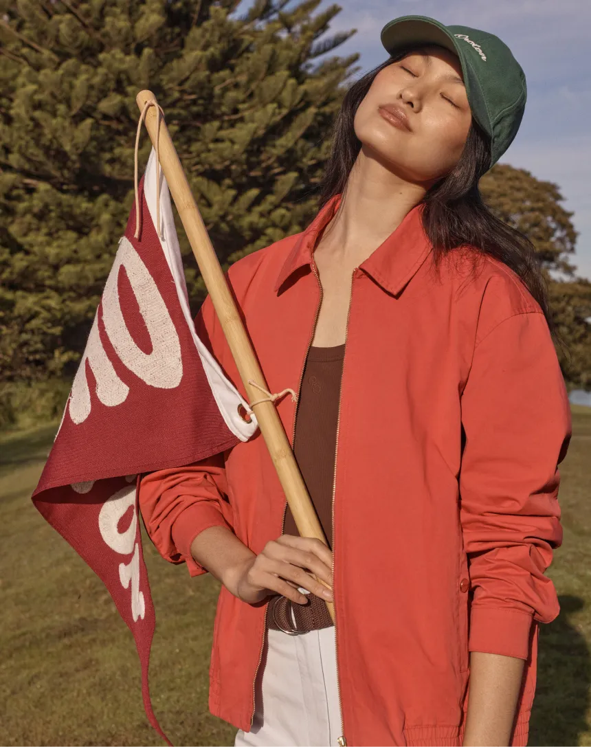 Person holding a flag outdoors, wearing a green cap and red jacket.