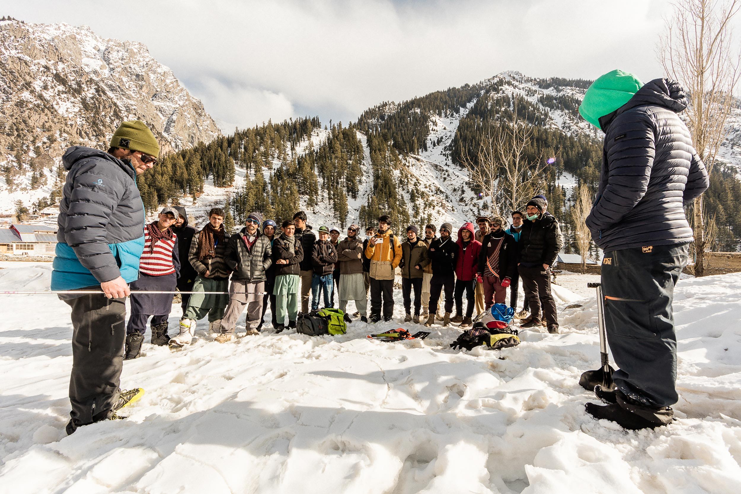 Group of people gathered in snow with mountains in the background.