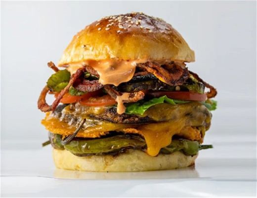 A tall burger with layers of meat, cheese, vegetables, and sauce.
