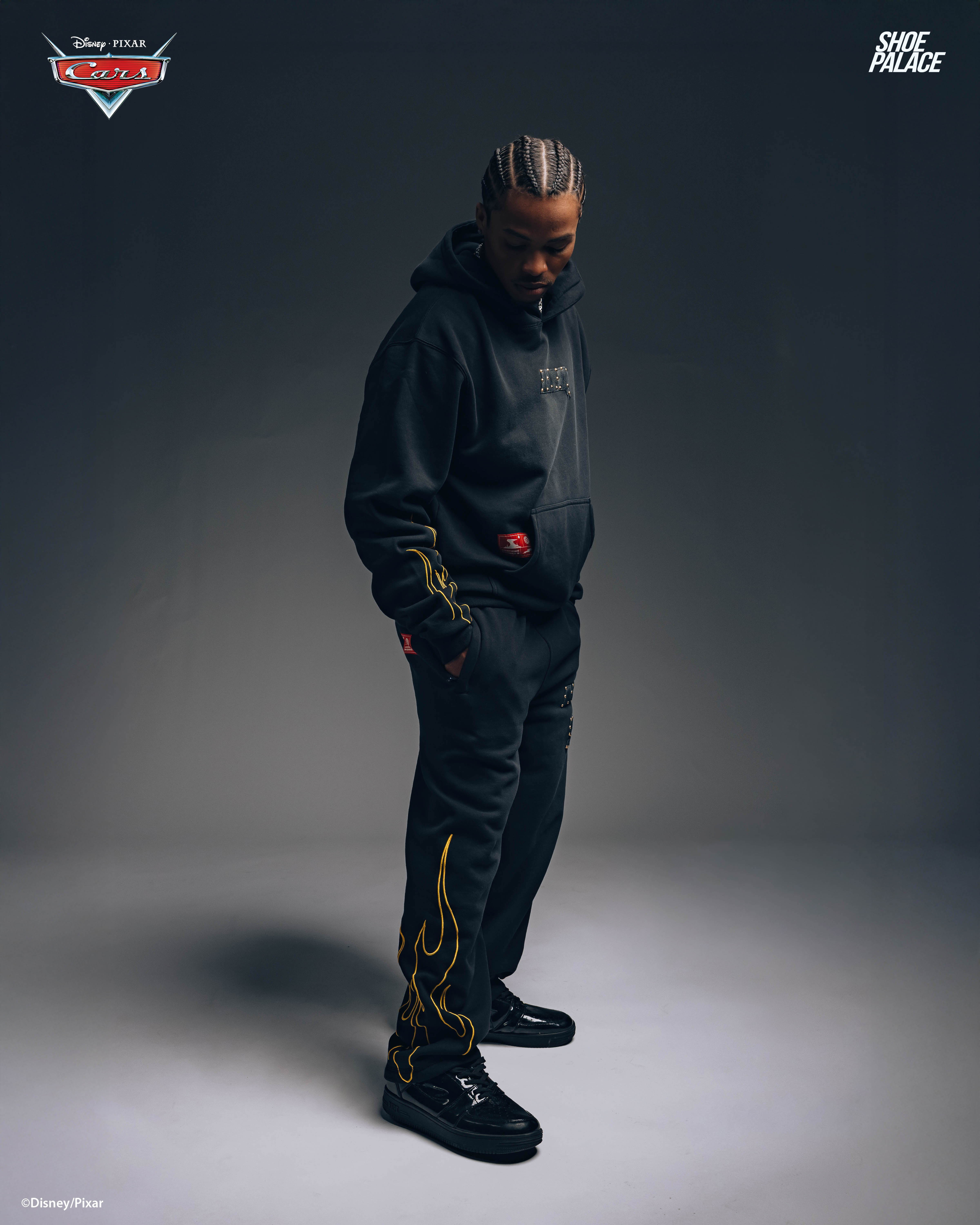 Person wearing black hoodie and pants, standing in a dimly lit space.