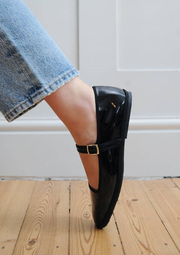 A styled image of a model foot on point wearing the Drogheria Crivellini Patent Mary Janes in black.