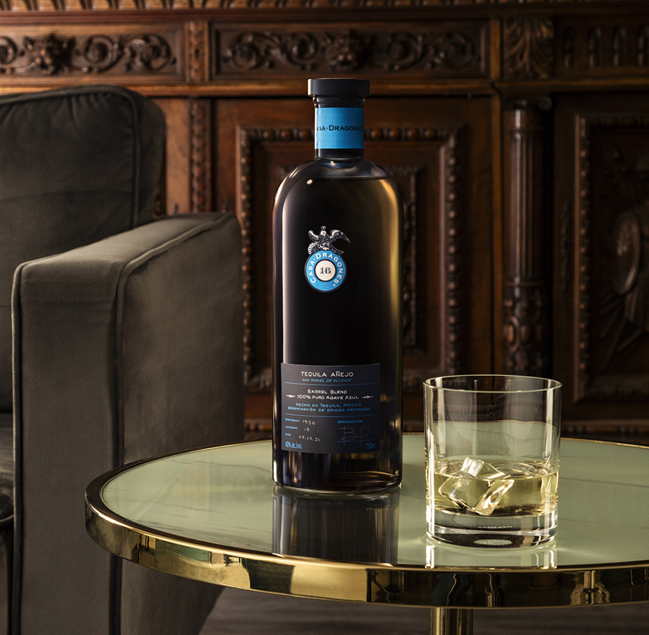 Bottle of liquor next to a glass with ice on a table.