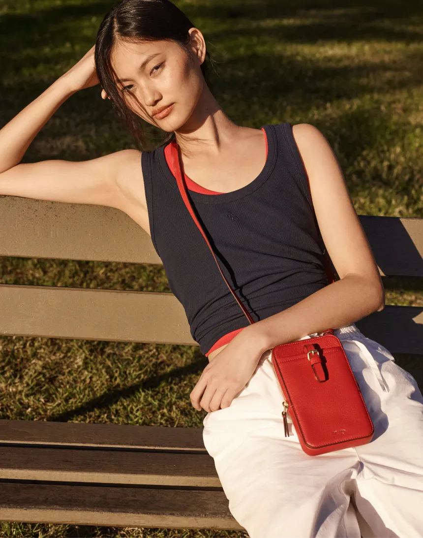 Young woman in casual attire sitting on a bench, holding a red bag.