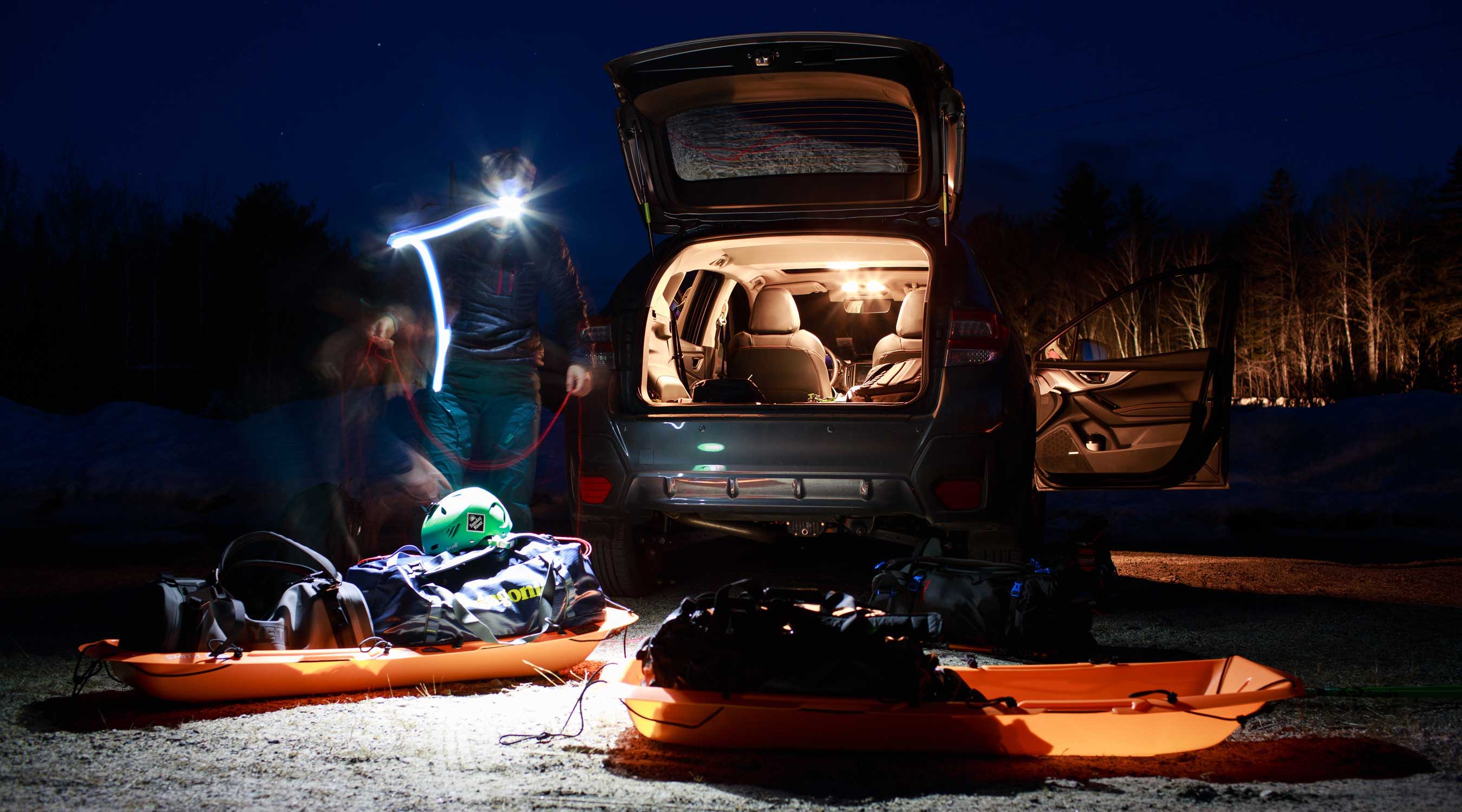 Person preparing gear next to a car at night, illuminated by a light.