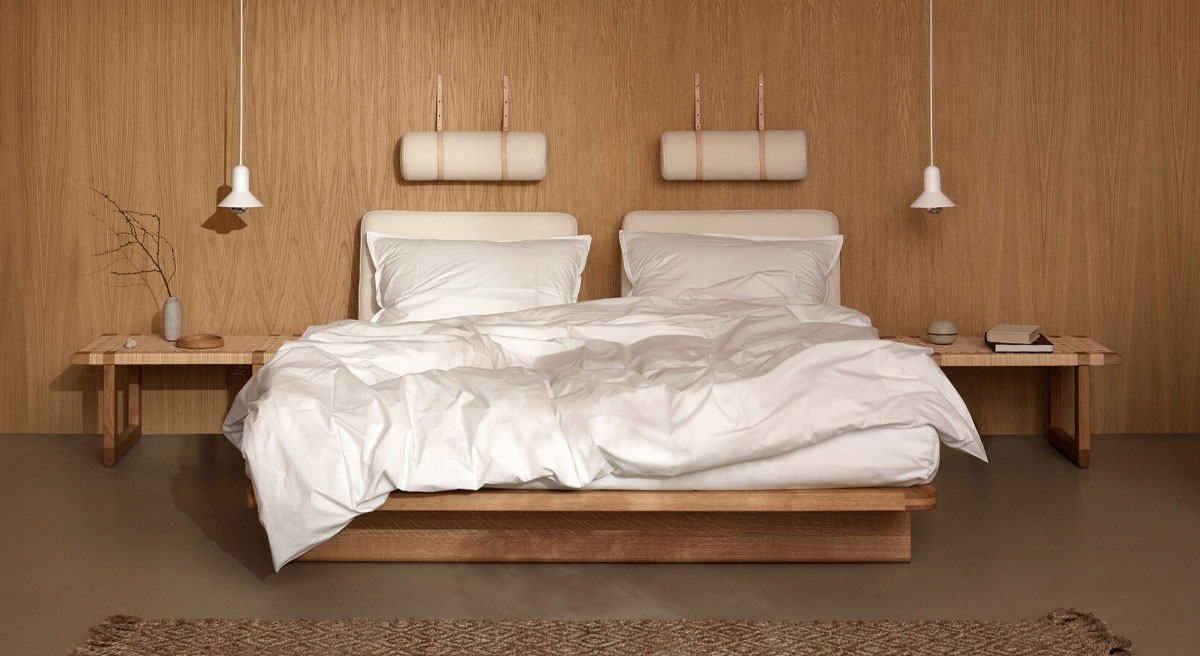 Modern bedroom with wooden walls, Carl Hansen bed, and minimalist decor.