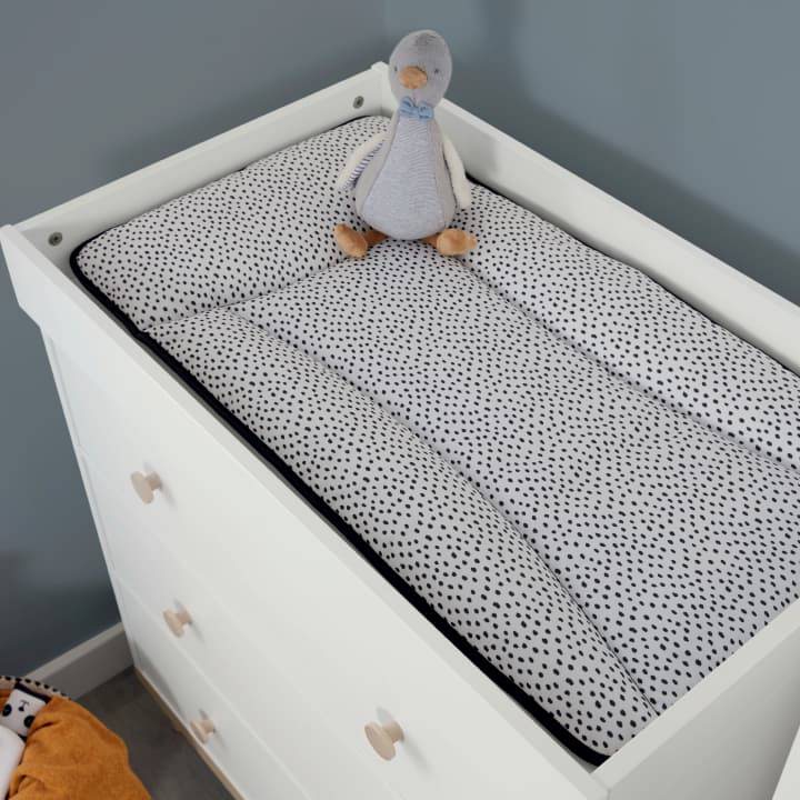 A black and white spotted changing mat sits on a dresser changer with a small duck soft toy on top.