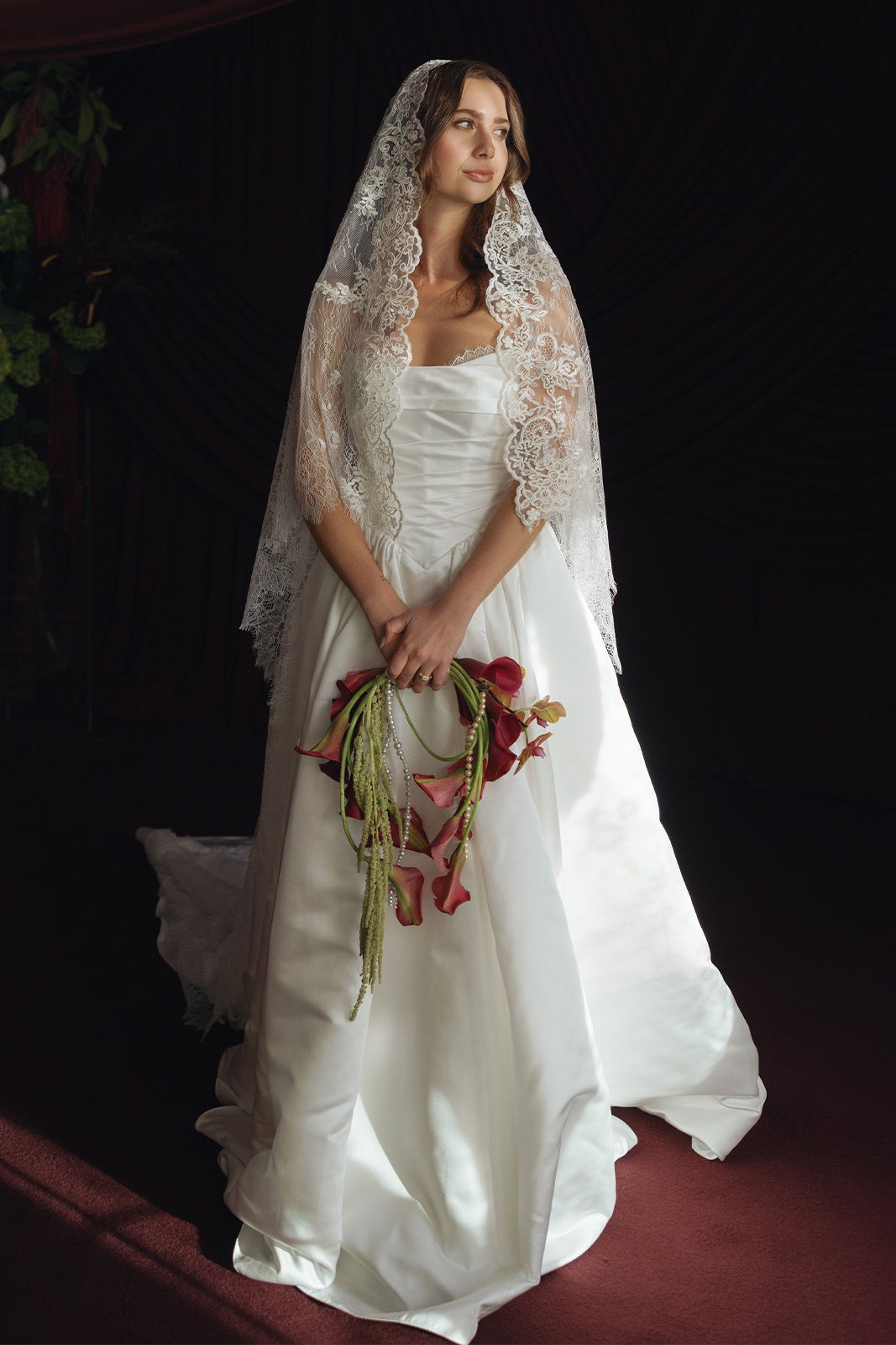 Bride in elegant wedding dress holding a bouquet, wearing a lace veil.