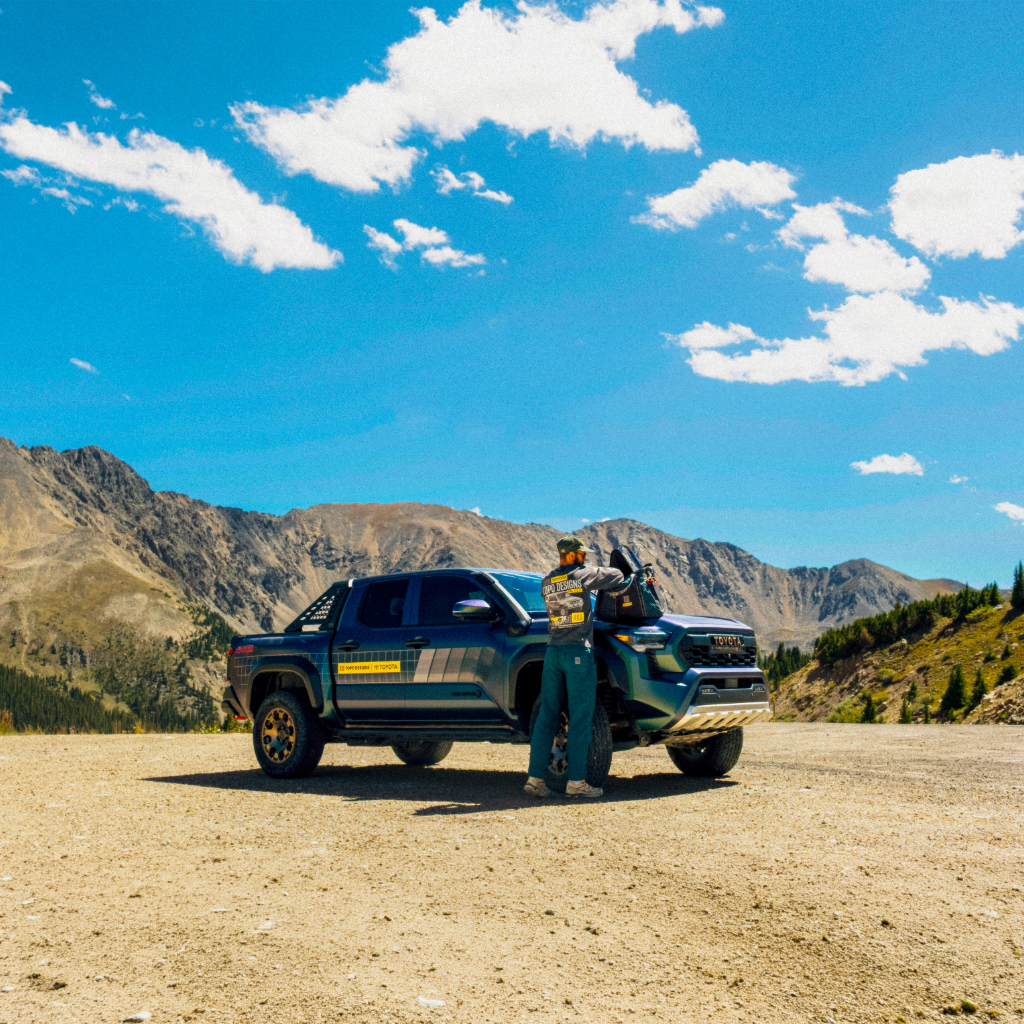 Person standing next to a truck in a mountainous outdoor setting.