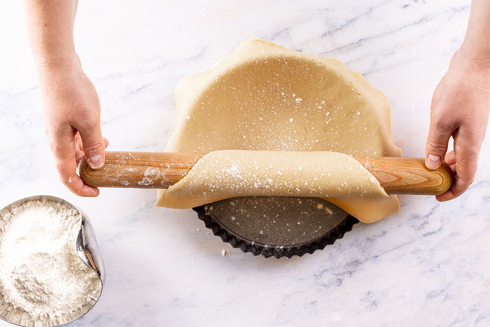 Person rolling out pie dough with a rolling pin on a marble surface.