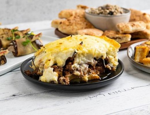 A plate of layered meat and cheese dish with various sides.