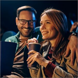Smiling couple enjoying a movie with popcorn and drinks in a theater.