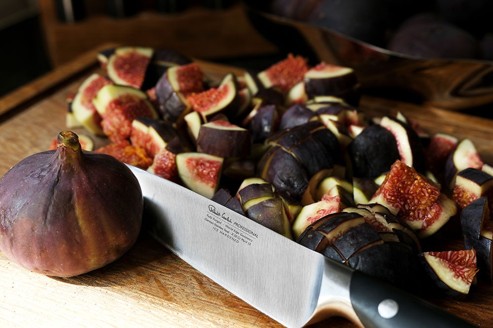 A Professional Knife beside sliced figs on a wooden cutting board.