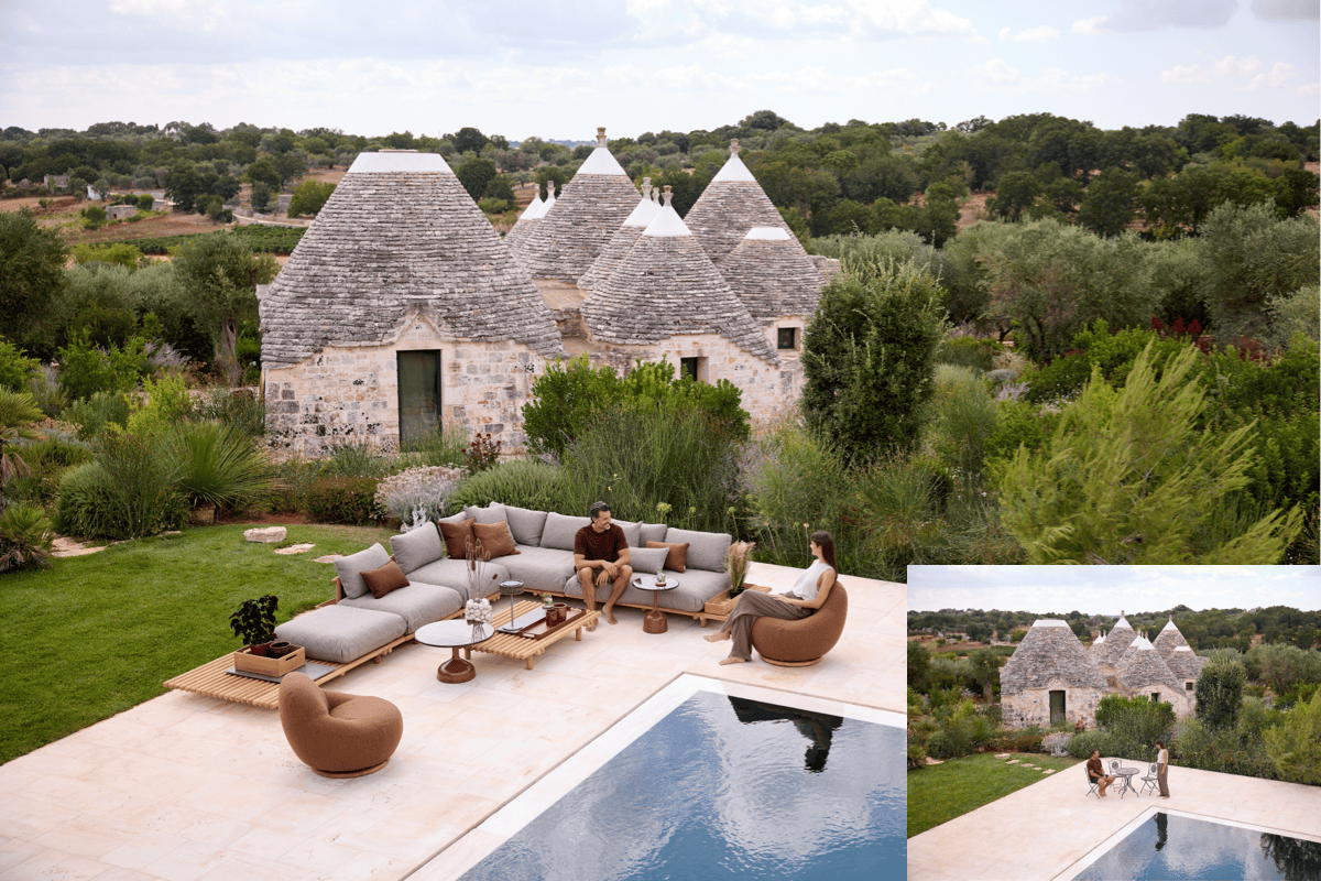 Luxury pool terrace with low-profile sectional seating, wood slat platforms, rounded upholstered lounge chairs, and a stone patio overlooking traditional trulli buildings.