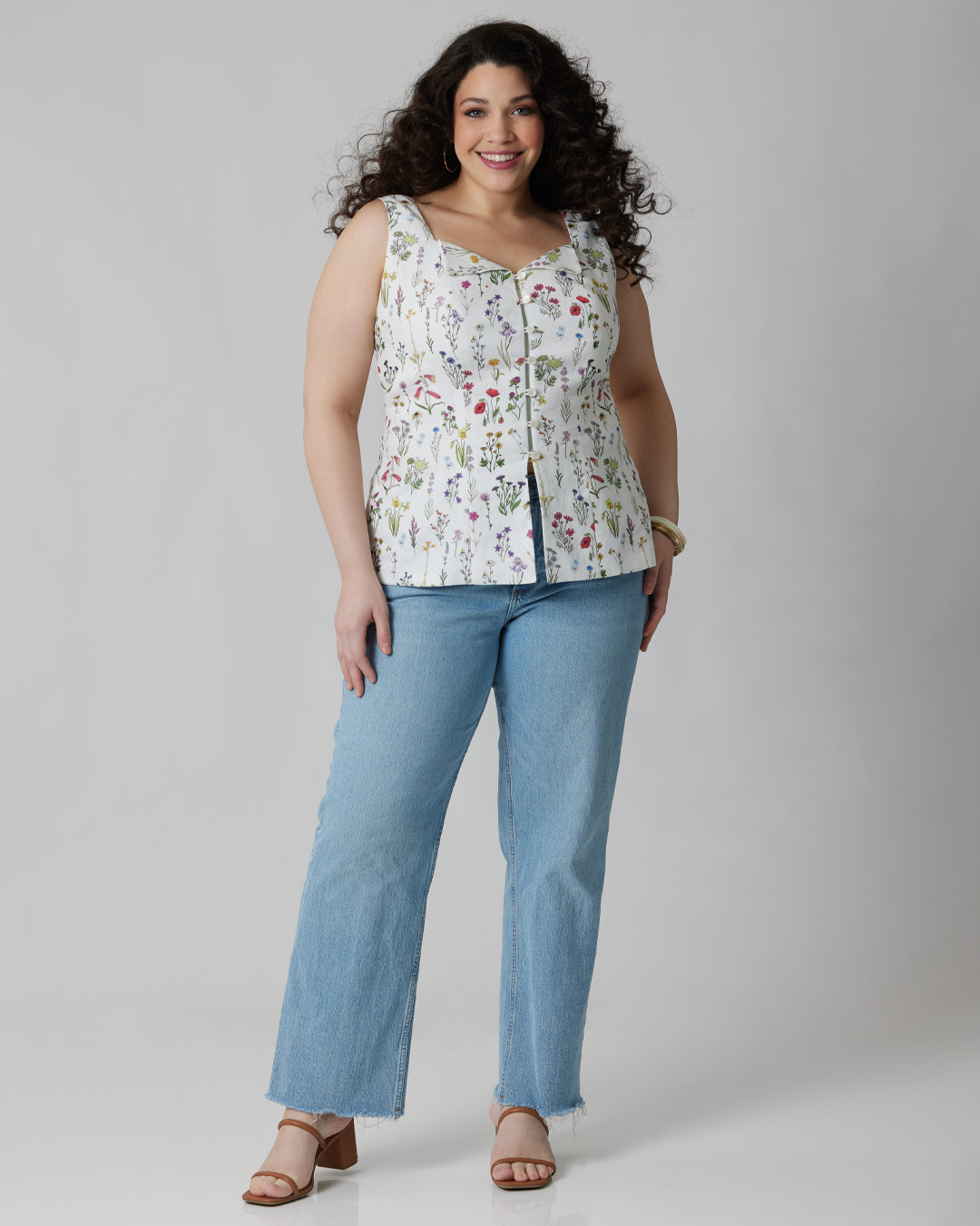A woman with curly hair wearing a floral top and jeans.