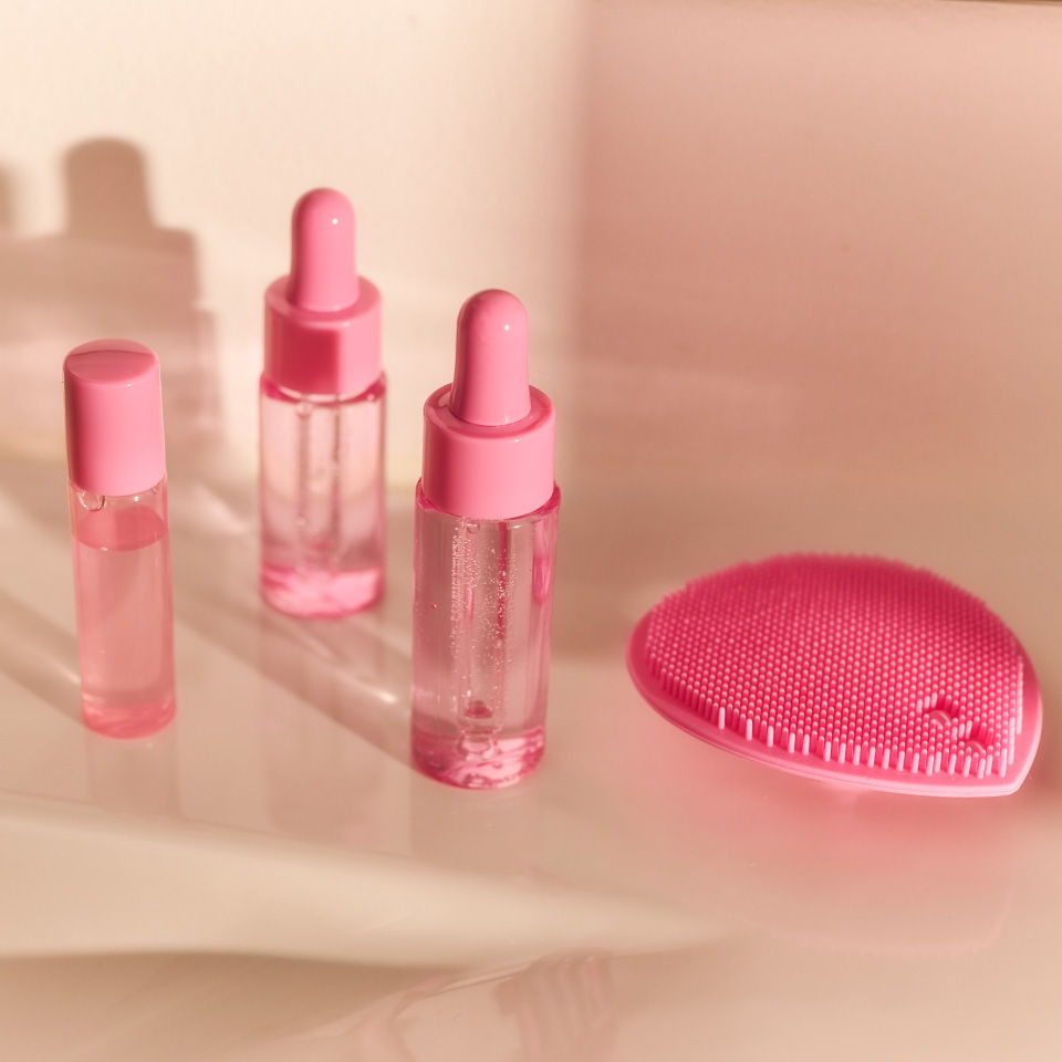 Three pink glass bottles and a pink compact on a light background.