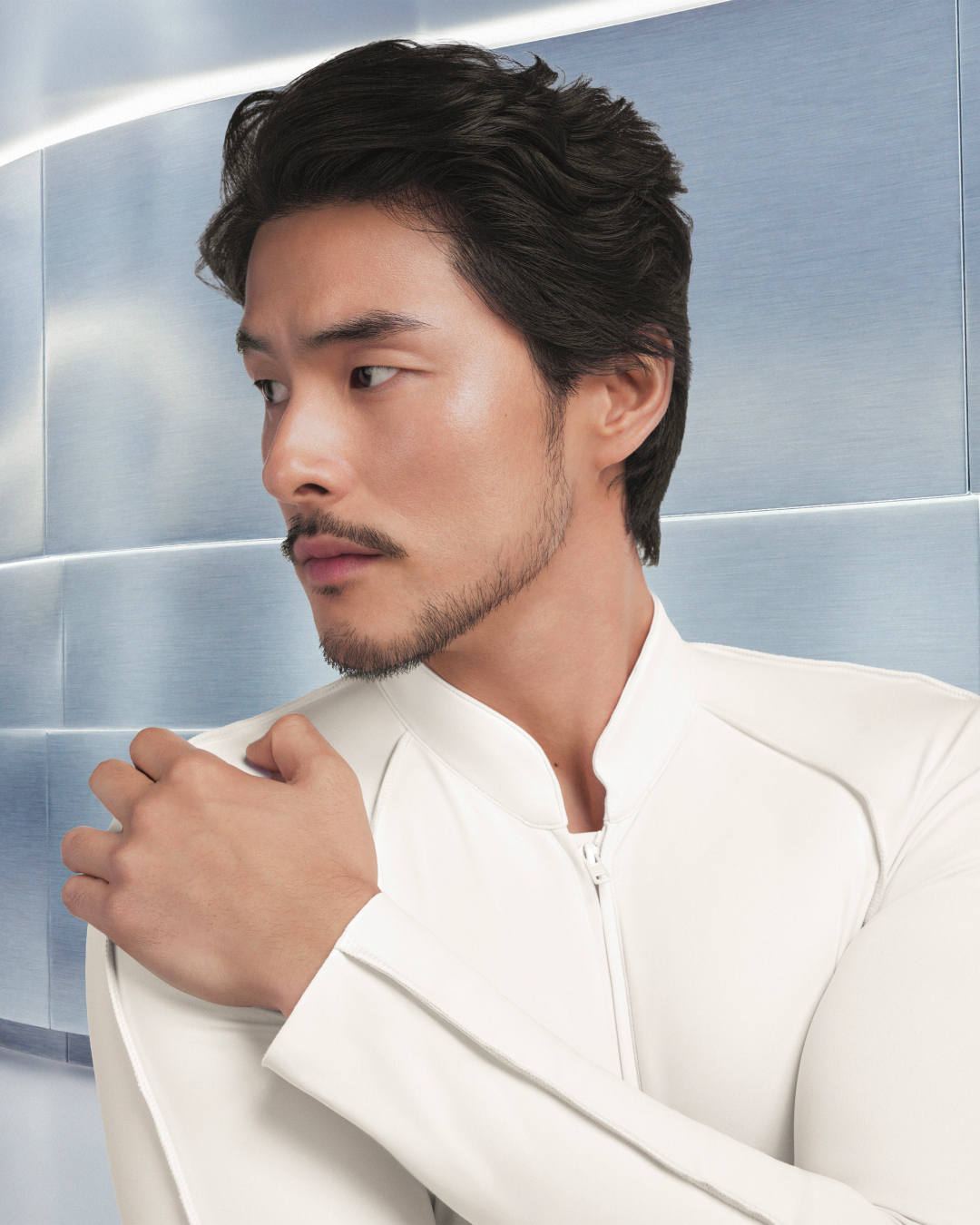 A man in a white outfit poses against a light blue background.