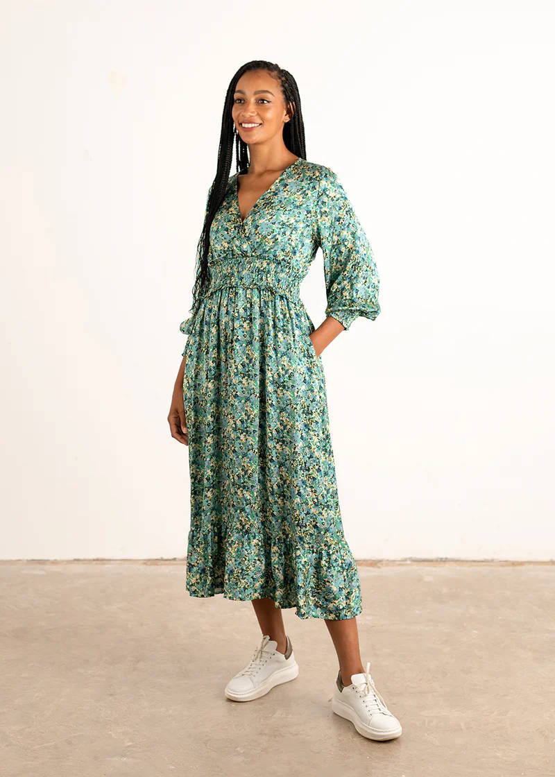 A model wearing a green and blue  floral print satin midi dress with long sleeves and white trainers