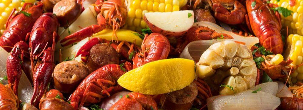 a close up of a crayfish boil with lemon, garlic bulb, corn, potatoes, and onion