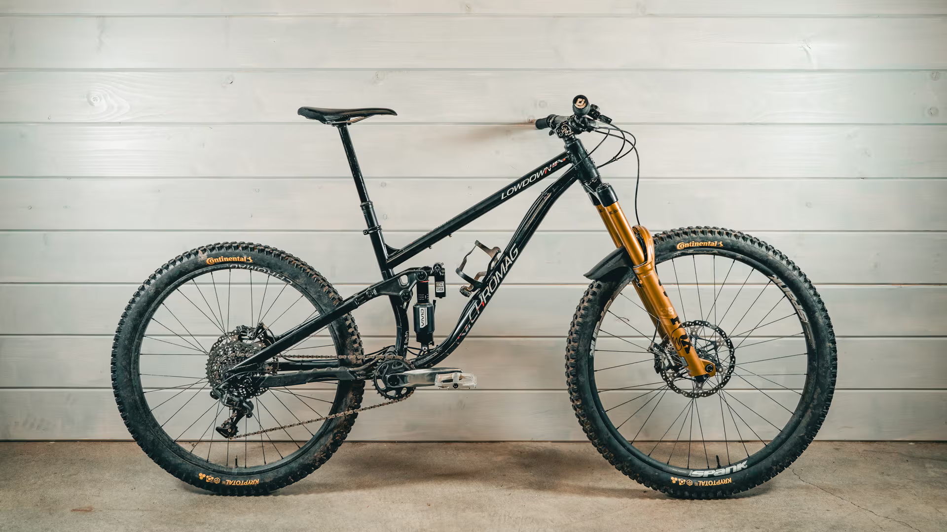 Mountain bike with a black frame and gold suspension fork against a wooden background.