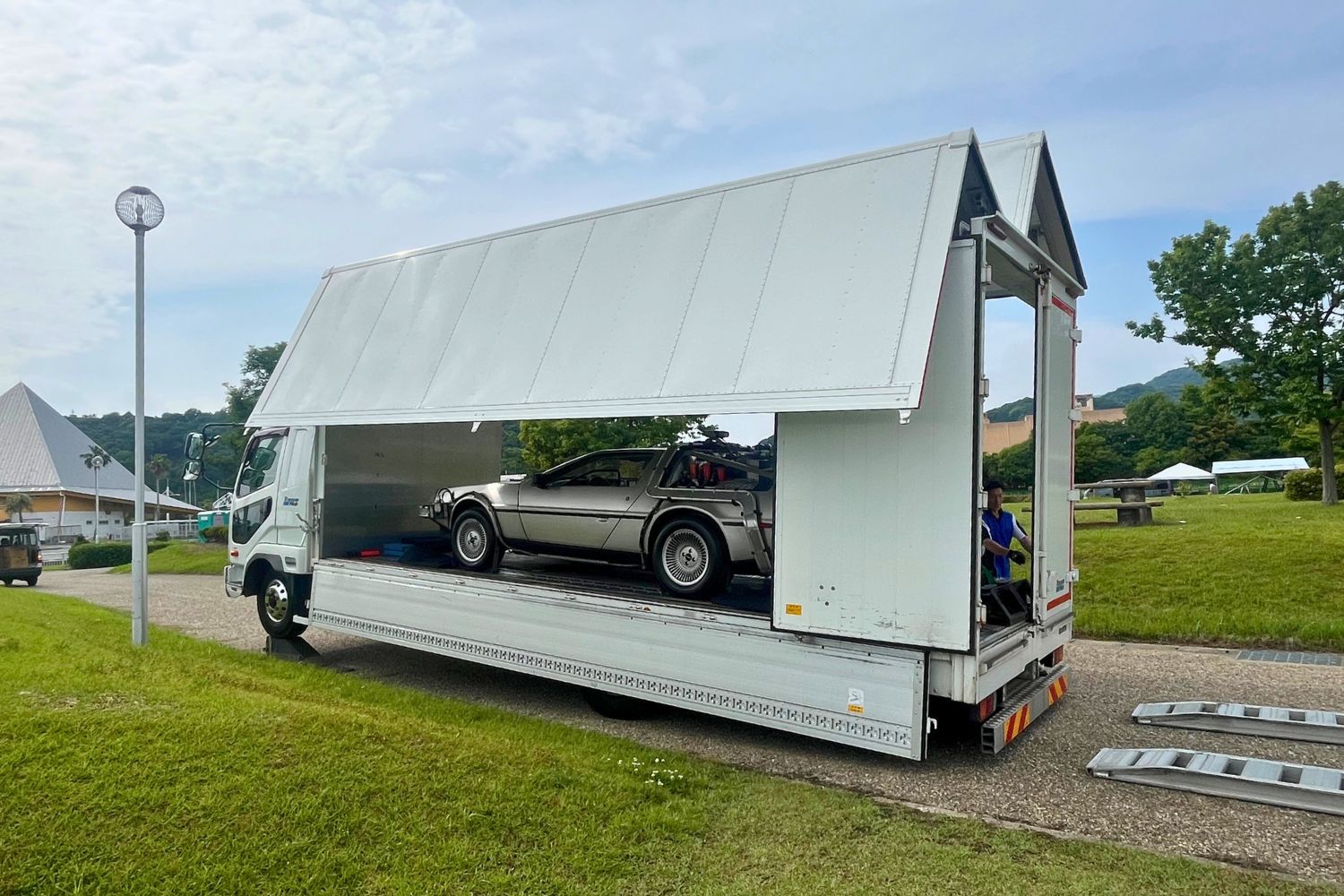 Truck transporting a car with an open top, parked on grass.