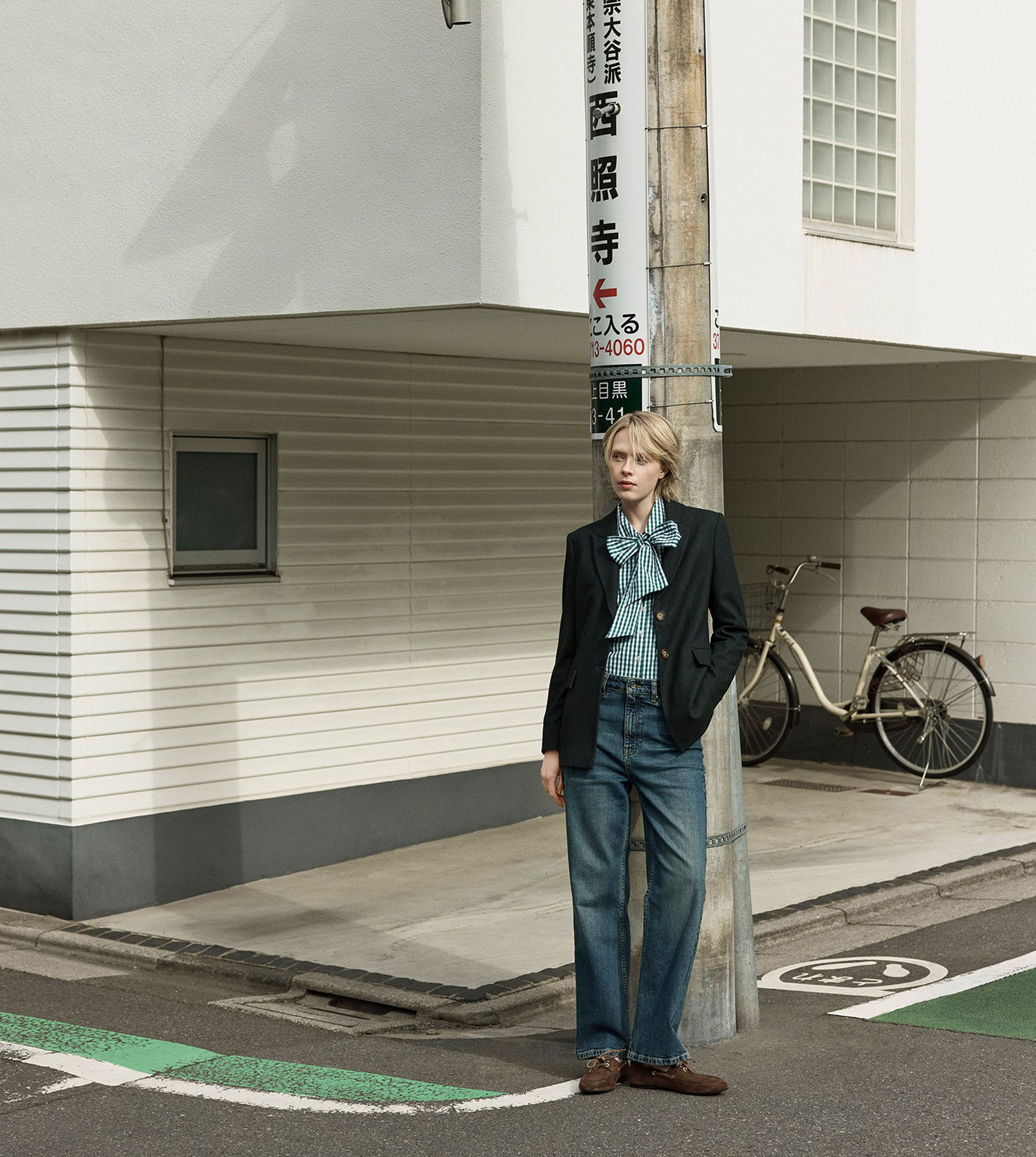 Person in stylish attire standing near a building and bicycle.