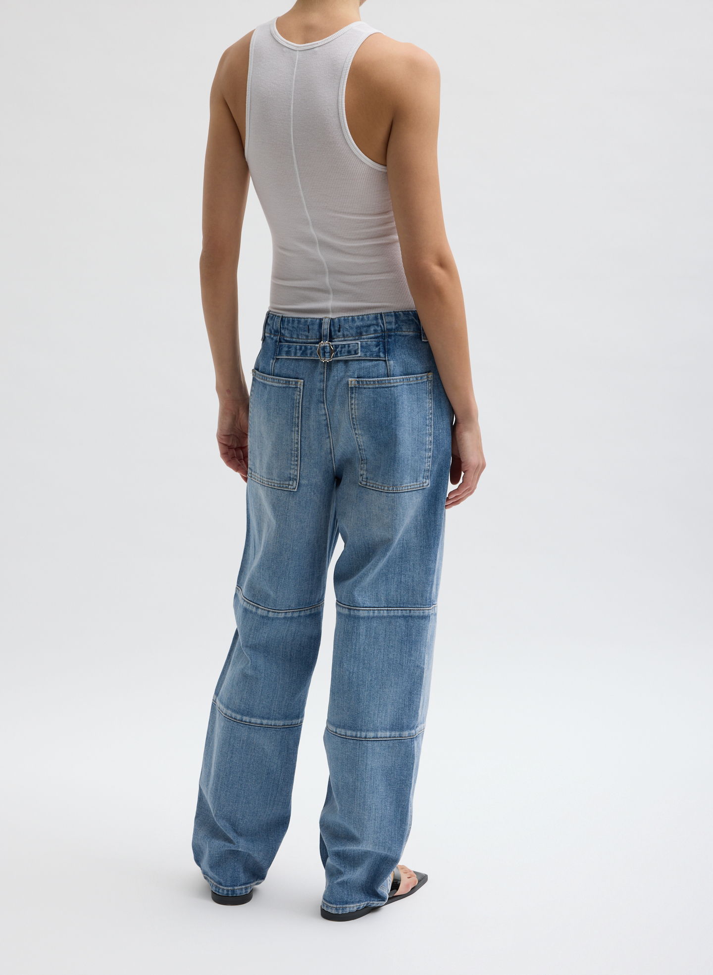 Person wearing a white tank top and blue jeans, viewed from behind.