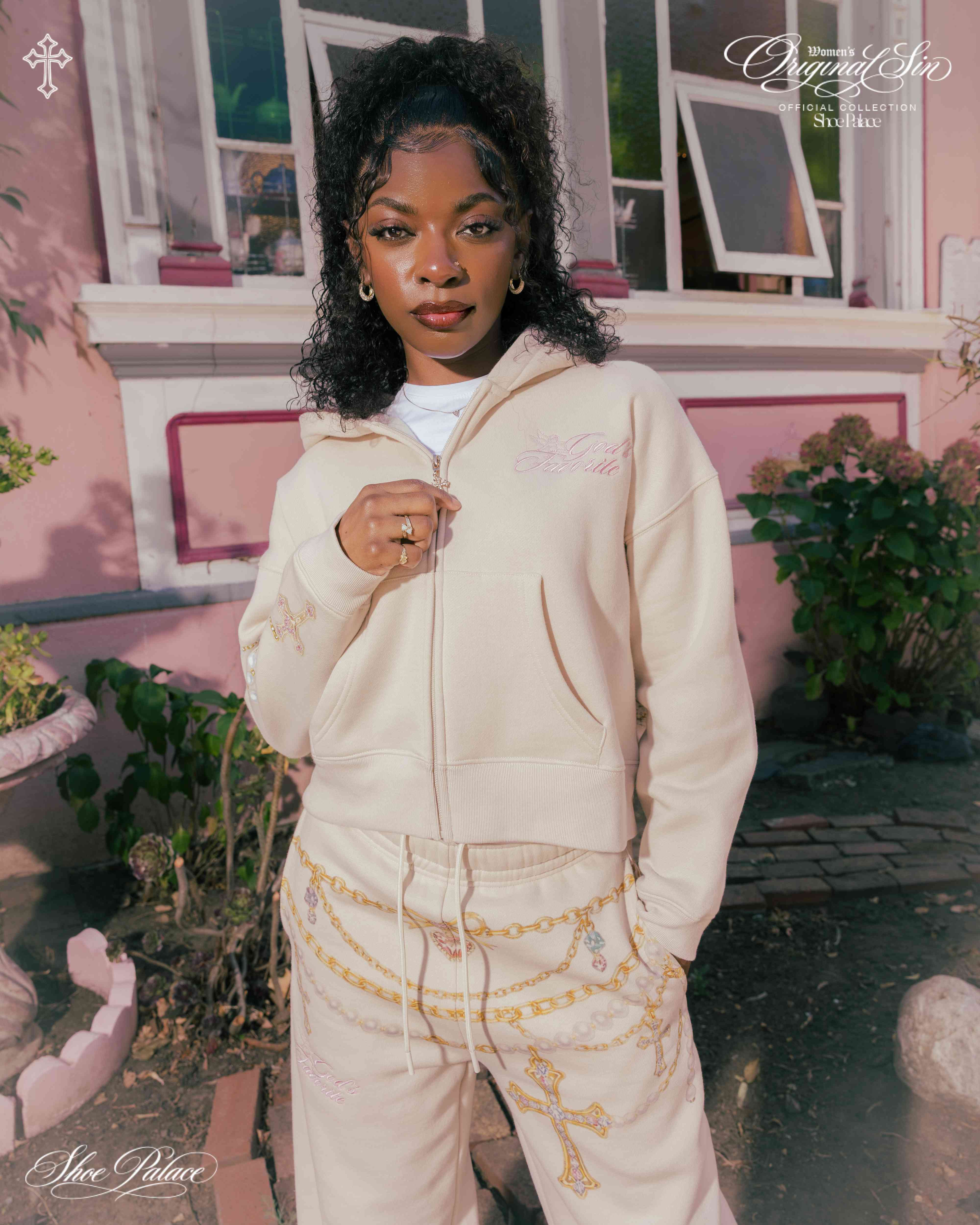 Person in a beige outfit standing in front of a pink building.
