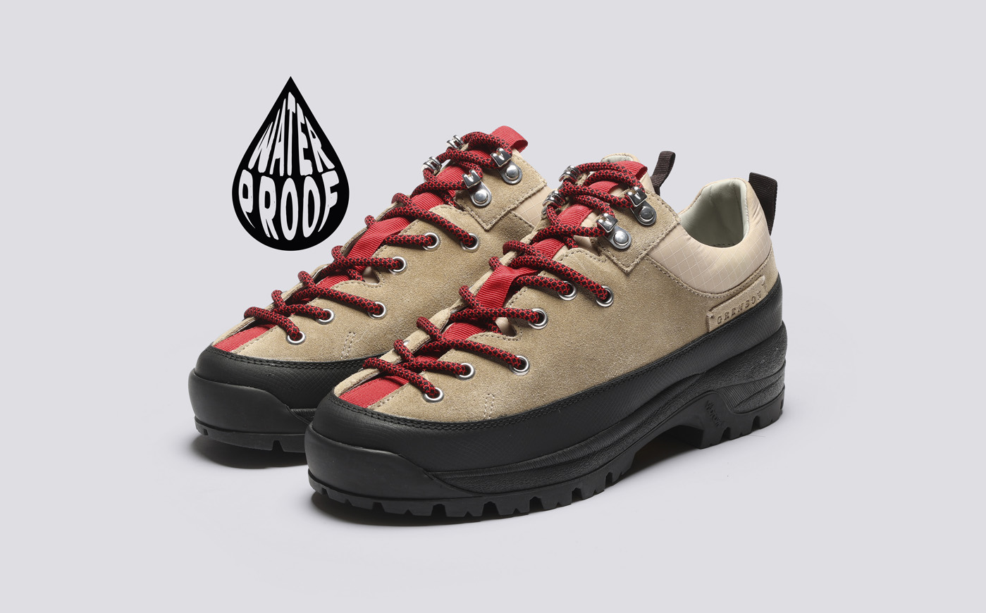 Grenson Sneaker 70. Beige and black hiking shoes with red laces on a gray background.