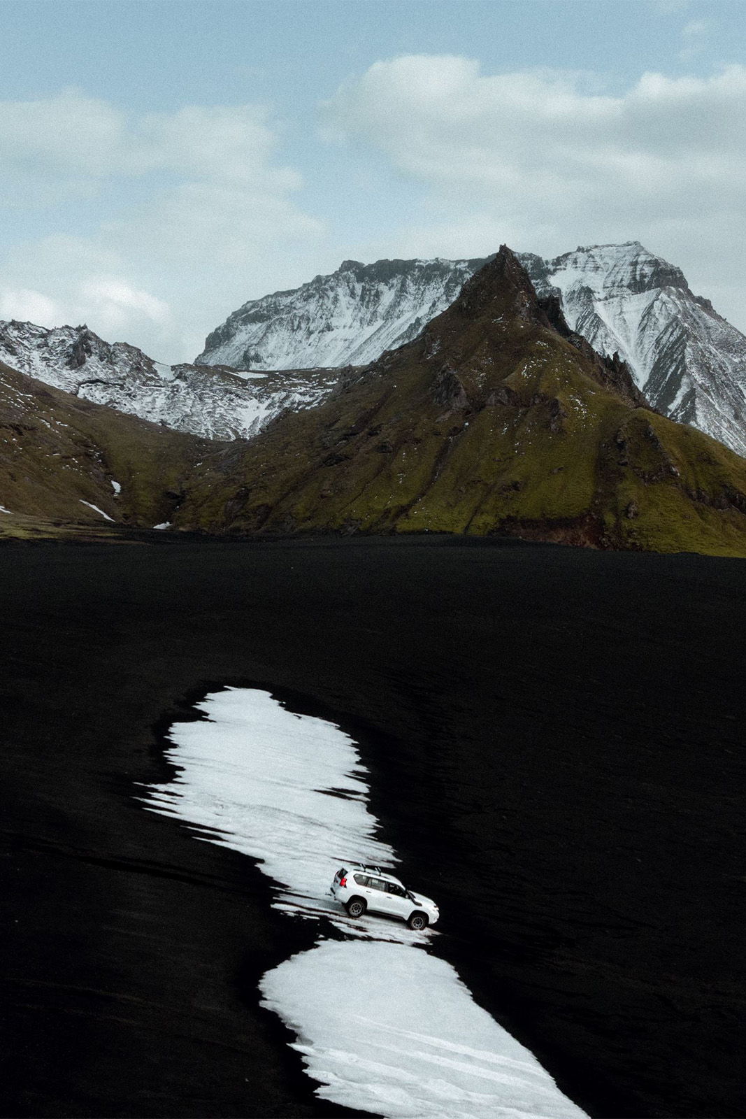 Snowy path on black volcanic landscape with mountains in the background.
