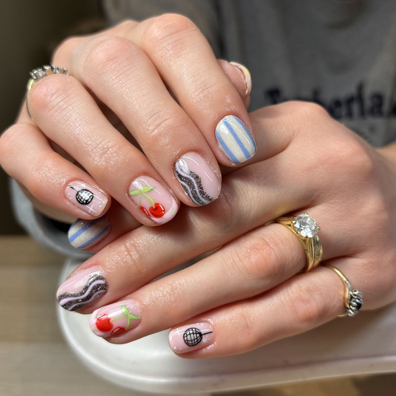 Colorful nail art design on hands with various patterns and rings.