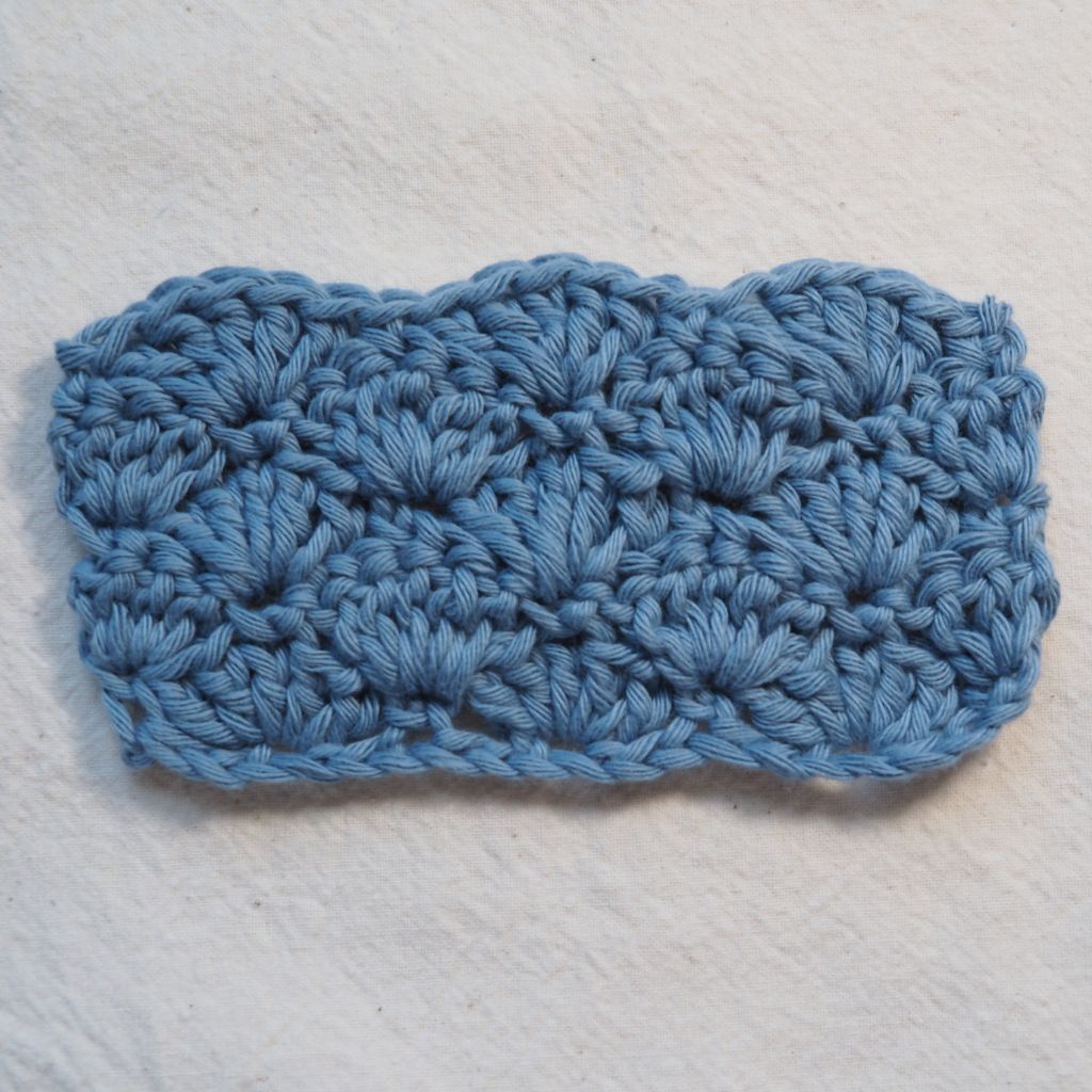 Maschenprobe die ein gehäkeltes Muschelmuster aus blauem Garn zeigt. 