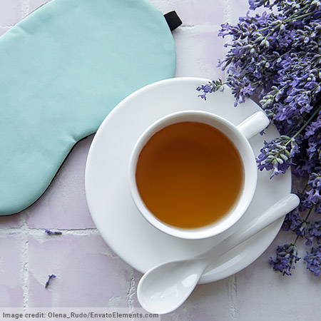 white saucer and teacup filled with tea, white teaspoon, light blue eyemask and fresh lavender sprigs on light tiled background