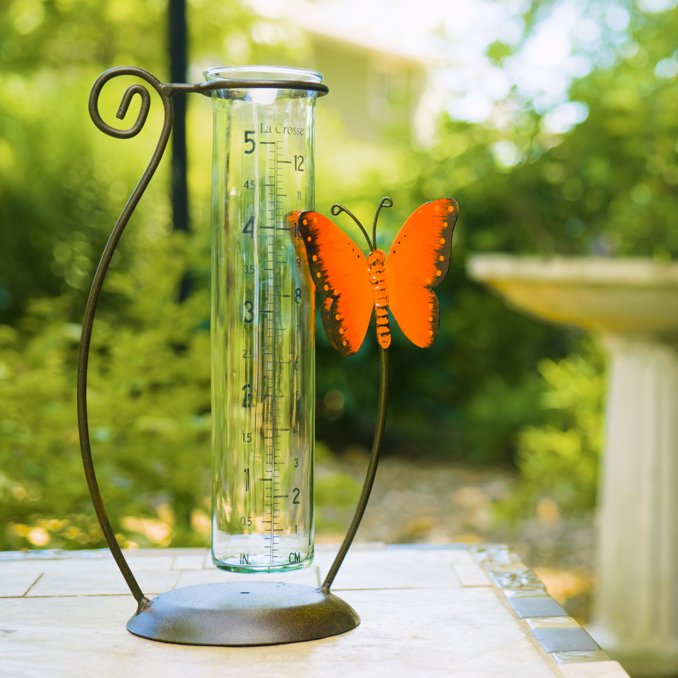 704-13077 Glass rain gauge with an orange butterfly decoration in a garden setting.