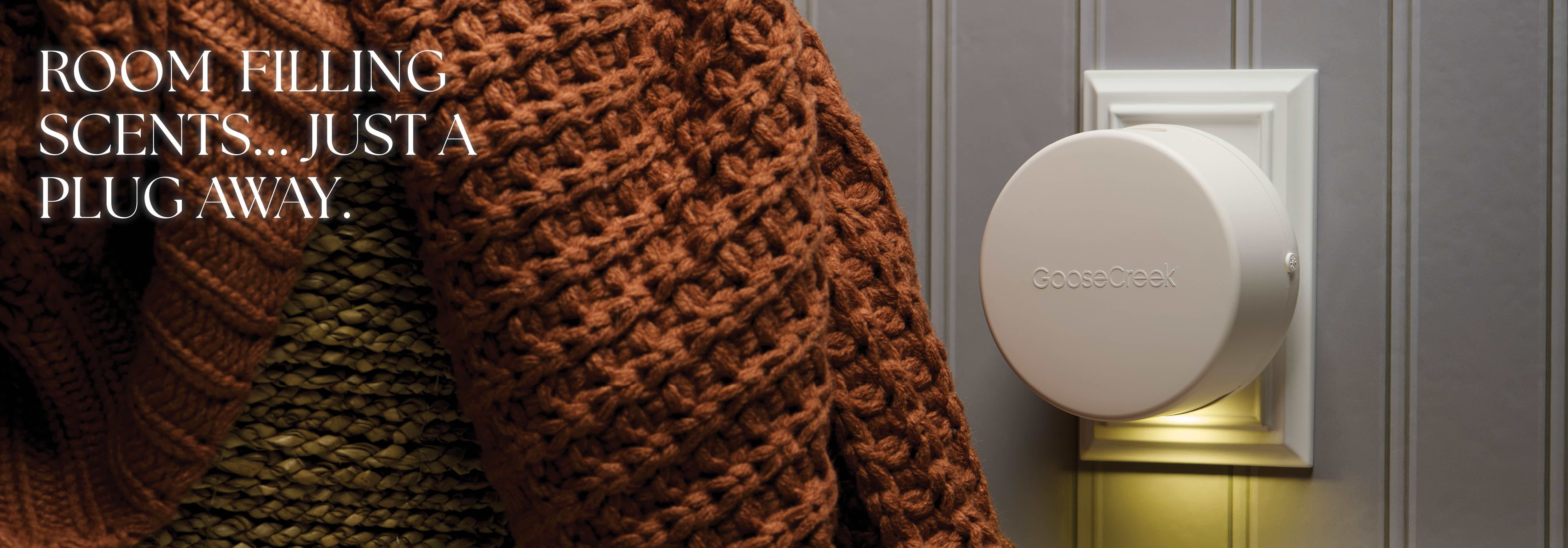 A person wearing a sweater next to a scent diffuser on the wall.
