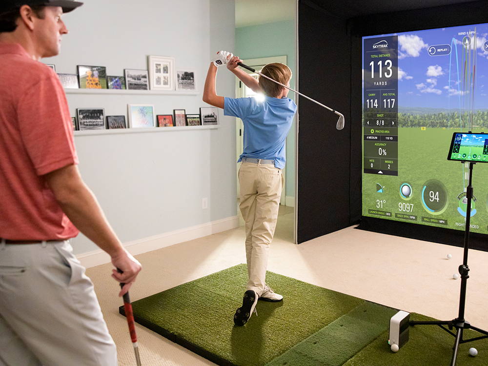 Man watching while a boy swings a golf club in a SkyTrak golf simulator