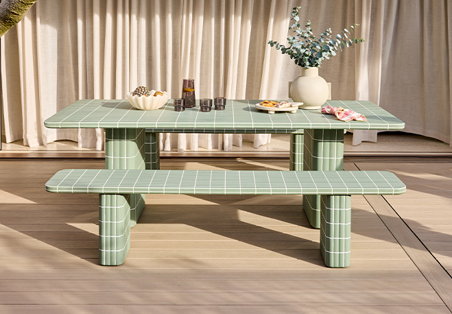 A green picnic table with a vase and snacks on a patio.