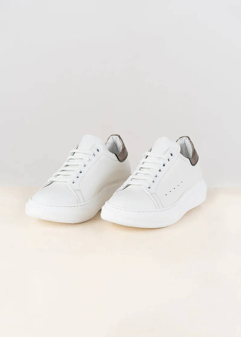 A pair of white leather trainers with a chunky sole and metallic detailing on the ankle