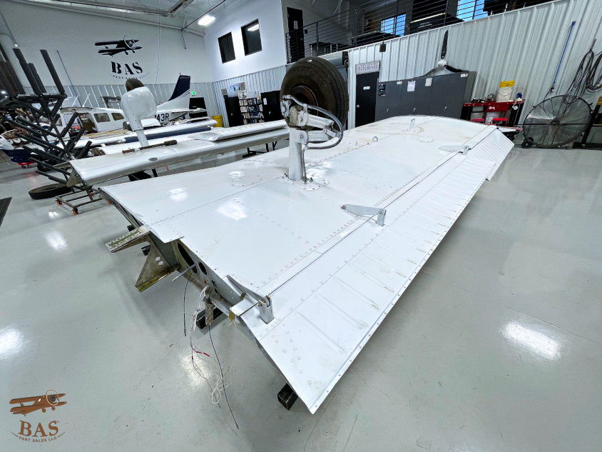 White aircraft wing in a workshop with equipment and tools visible.