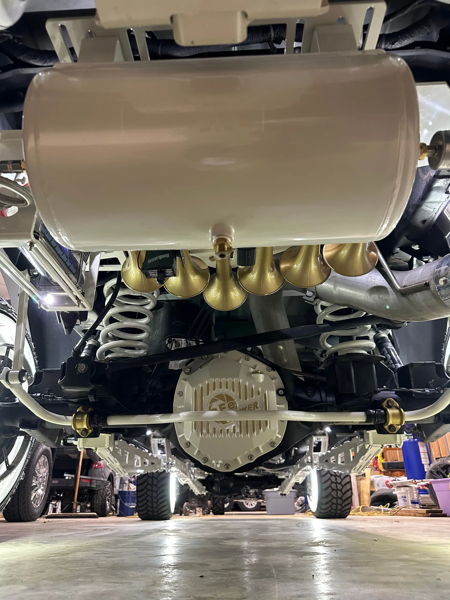 Underbody view of white air tank and six gold HornBlasters train horns above white PPE differential cover and suspension