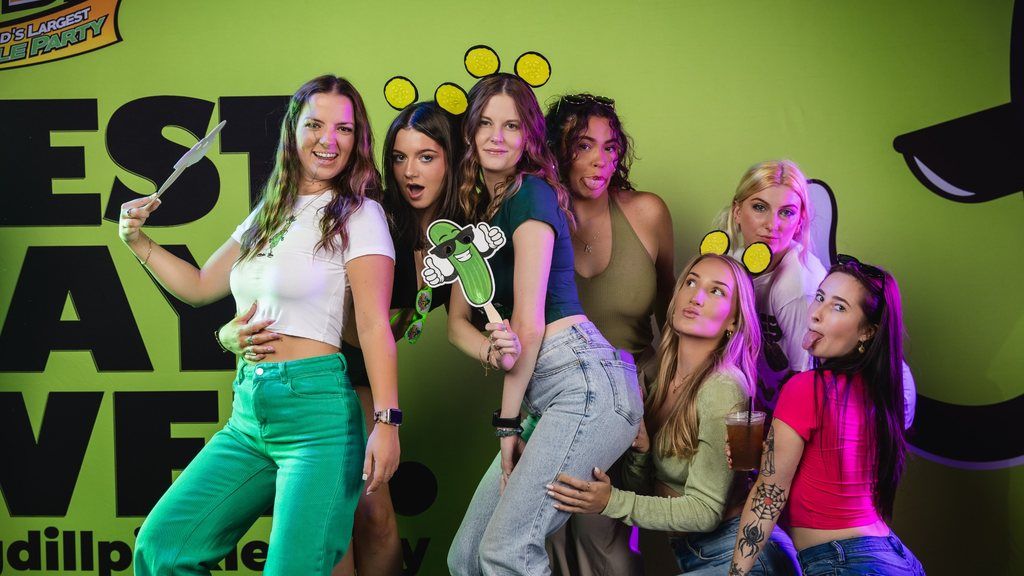 Group of friends posing in the photo booth with a Dilly the Pickle® cutout at The Big Dill® Baltimore 2025 pickle festival