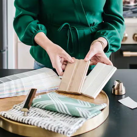 Person holding fabric swatches and samples on a table.