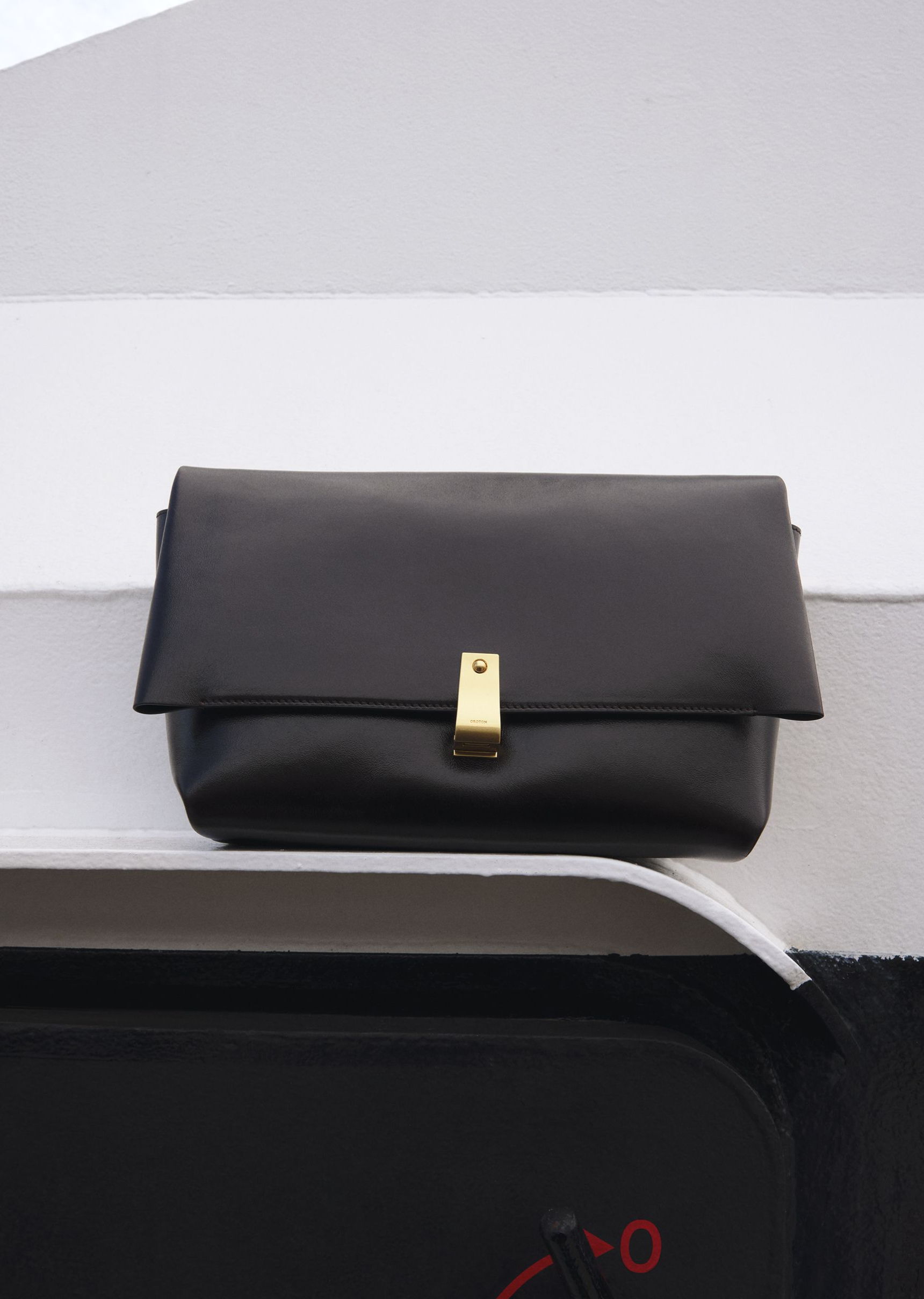 A black clutch bag with a gold clasp resting on a surface.