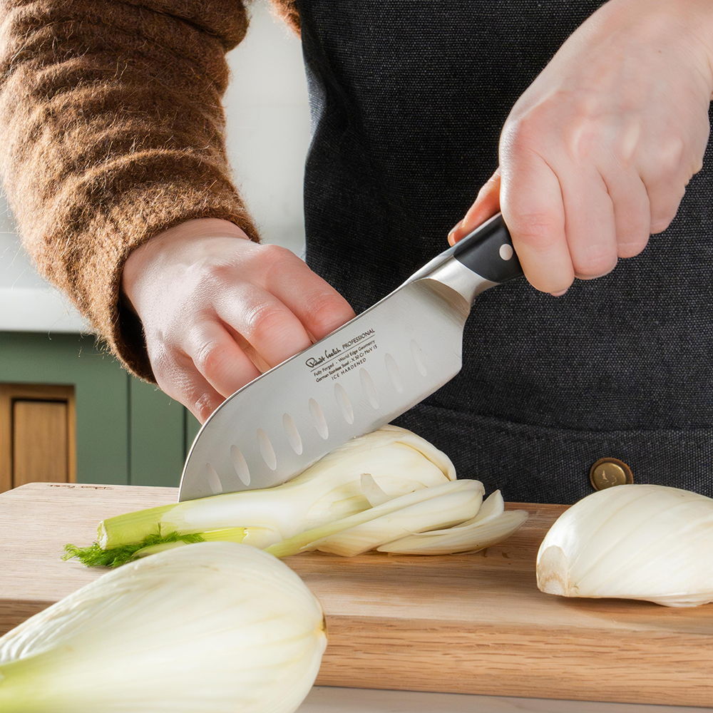 Person slicing vegetables on a wooden cutting board with the Professional Santoku knife.