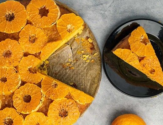 A cake topped with orange slices, served with a slice on a plate.