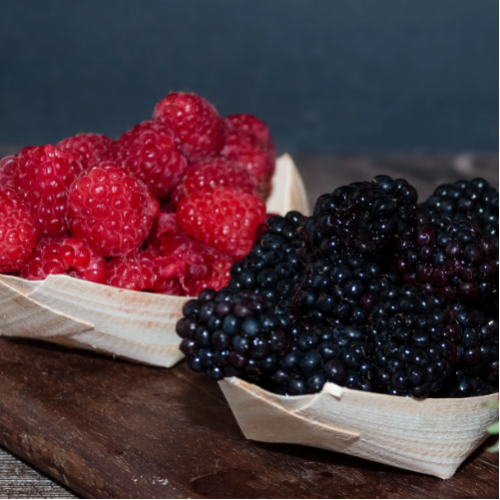 Two wooden baskets filled with red raspberries and blackberries on a wooden surface.