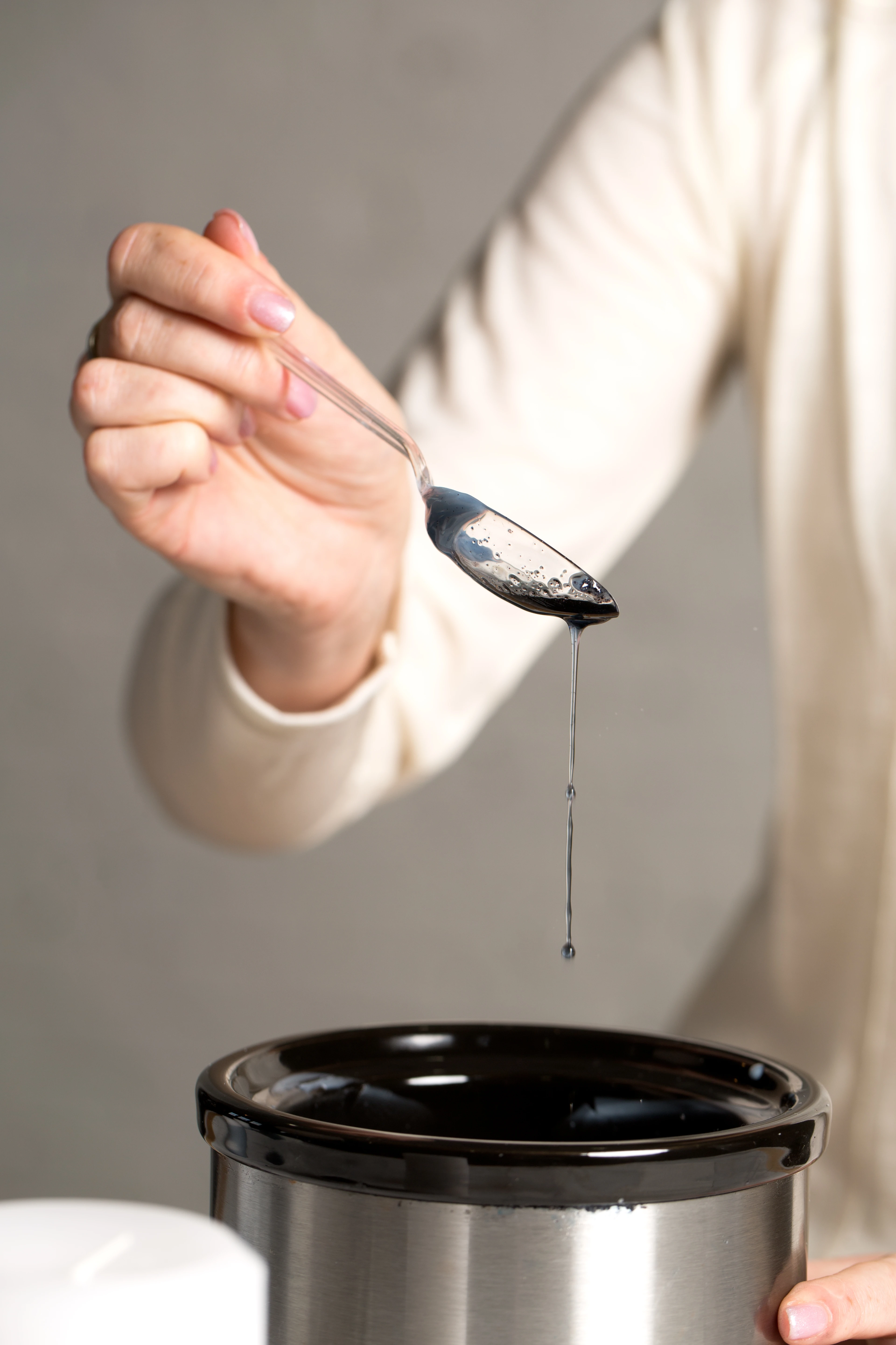 Hand holding a spoon with liquid dripping over a container.