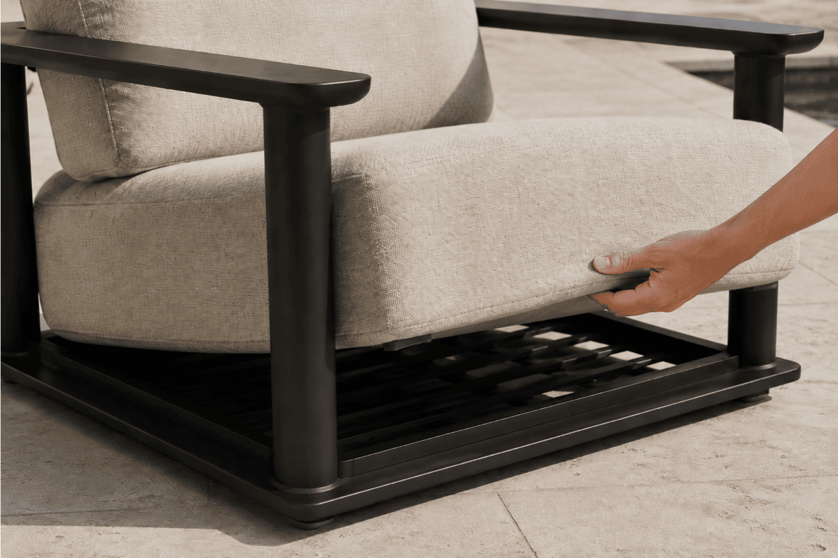 Outdoor lounge chair detail showing a thick performance cushion lifted to reveal concealed drainage slats