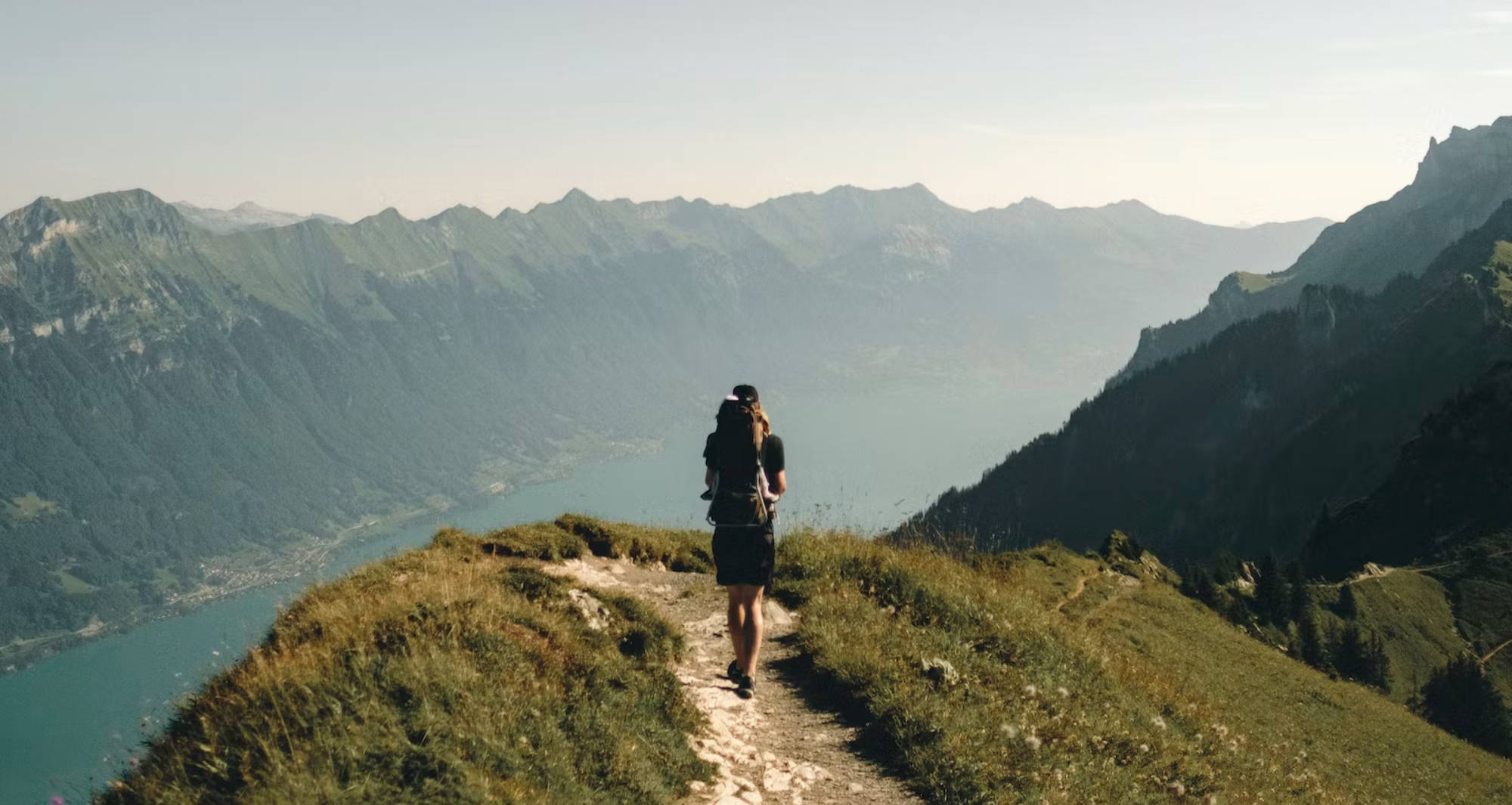  a person hiking on a thin path high above a laken surrounded by mountains